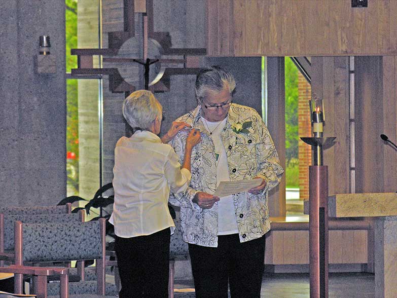 Joyce Fruge presents the Associate logo lapel pin to Mary Veen.